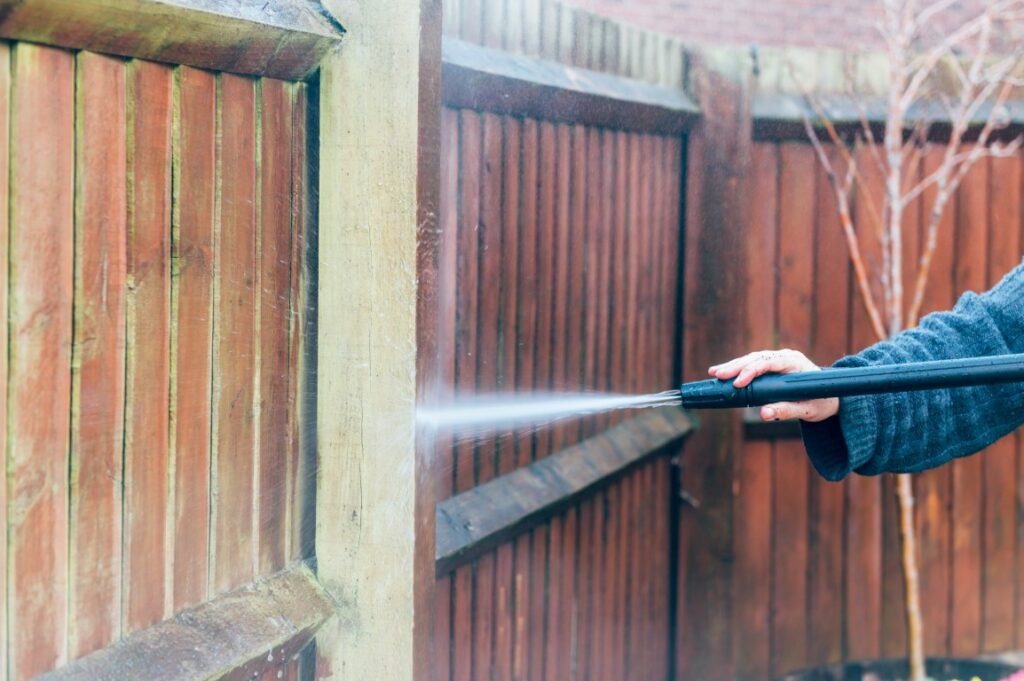 Closeup of a person cleaning a wood fence with a pressure washer.