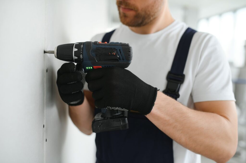 A man installing drywall with an electric screwdriver.